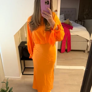 Orange långklänning med knytärmar - Säljer en snygg orange långklänning med långa ärmar och knyt vid ärmsluten. Klänningen har en elegant och flytande design som ger en fin silhuett. Passar perfekt till bal eller andra festligare tillfällen 🧡🥰
