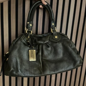 Marc Jacobs väska  - Marc Jacobs classic q baby groove med guldiga detaljer. Väskan är mörk grön. Axelremband ingår. Den är ca 40 cm bred och är i den större modellen. Okej skick. Fler bilder finns och svarar gärna på frågor. OBS se bilder för de slitningar som finns på lädret 💚