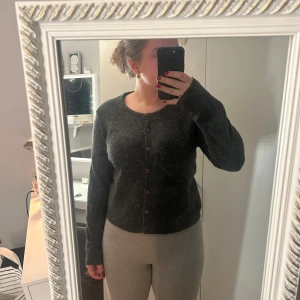 Mörkgrå kofta med knappar - Säljer en mysig mörkgrå kofta med knappar framtill. Koftan har långa ärmar och en klassisk design som passar perfekt för kyligare dagar. Perfekt att ha över en topp eller klänning för extra värme.