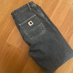 Blå jeansbyxor från Carhartt - Säljer ett par klassiska blå jeansbyxor från Carhartt med en praktisk bakficka och märkets logga. Perfekta för en avslappnad stil och tillverkade i slitstarkt material.