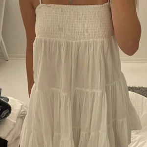 Vit axelbands klänning - Säljer en söt vit axelband klänning med volanger.