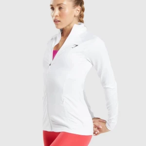 Vit träningsjacka från Gymshark - Snygg och funktionell vit träningsjacka från Gymshark med dragkedja framtill. Jackan har en tight passform och långa ärmar, perfekt för träning. Den är tillverkad i ett lätt och stretchigt material som ger bra rörelsefrihet. Använd en gång