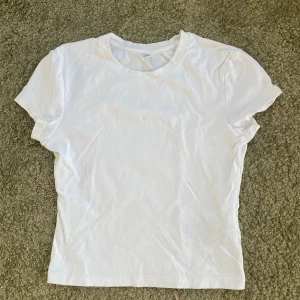 Vit baby tee från Uniqlo - Säljer en klassisk vit t-shirt från Uniqlo i storlek XS. Den är tillverkad i mjukt bomullsmaterial och har en rund halsringning. Perfekt basplagg för alla tillfällen.