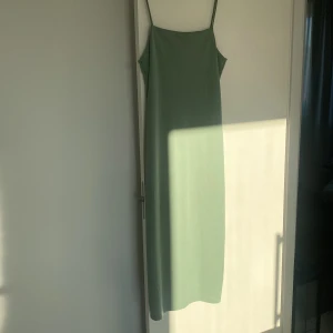 Grön långklänning från H&M - Säljer en stilren grön långklänning från H&M med smala axelband och en elegant slits. Perfekt för en somrig look. Klänningen har en enkel och tidlös design som passar till många tillfällen. 🌿