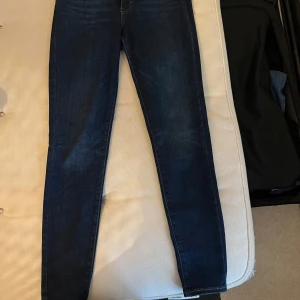 Mörkblå Levis jeans - Snygga mörkblå Levis jeans i modellen Mile High Super Skinny. De har en hög midja och en tight passform som framhäver benen. Klassiska bakfickor med Levis ikoniska sömmar och en liten röd etikett. Perfekta för en stilren look.