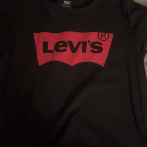 Svart t-shirt från Levi's - Säljer en svart t-shirt från Levi's med det klassiska röda logotyptrycket på framsidan. Perfekt för en casual look. 