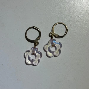 Blommiga örhängen i guld - Snygga örhängen med guldfärgade ringar och hängande blommor. Blommorna är ”transparanta” i en lila och glittrig ton