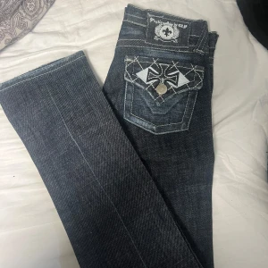 Mörkblå jeans med broderad bakficka - Snygga mörkblå jeans från Plastic by GLY med unikt broderi på bakfickan. Jeansen har en klassisk femficksdesign och kontrastsömmar som ger en cool look. Midjemåttet är 35 och innerbenslängden är 82. Står storlek 3 men skulle säga att dom passar xs/s 