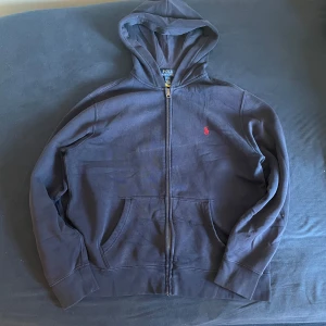 Navy hoodie från Ralph Lauren - Säljer en snygg blå hoodie från Ralph Lauren med dragkedja och röd logga på bröstet. Den är i barnstorlek L som motsvarar XS/S. Ställ gärna frågor om du är intresserad 