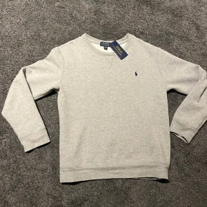 Grå Ralph Lauren hoodie  - Säljer en stilren grå sweatshirt från Polo Ralph Lauren. Med blå logga (ny) säljer pga ingen användning av det (14-16) xs