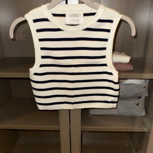 Randig ärmlös topp från Zara - Säljer en snygg ärmlös topp från Zara i vitt med svarta ränder. Toppen är ribbad och croppad, perfekt för en stilren look. Passar bra till både jeans och kjol.
