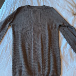 Brun stickad tröja - Säljer en stilren brun stickad tröja med ett diskret mönster längs framsidan. Tröjan har långa ärmar och en rund halsringning, perfekt för kyligare dagar. Passar både till jeans och mer uppklädda tillfällen.