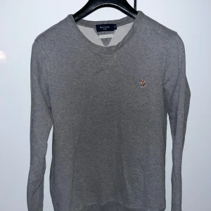 Grå tröja från Paul Smith - Säljer en stilren grå tröja från Paul Smith med ett broderat färgglatt zebramärke på bröstet. Tillverkad i 100% ekologisk bomull, vilket gör den både bekväm och hållbar. Nypris ca 1500kr.