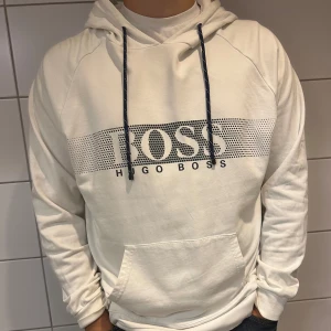 Vit hoodie från Hugo Boss - Säljer en snygg vit hoodie från Hugo Boss. Den har en stor logga på framsidan och justerbara snören i huvan. Perfekt för en casual look eller när du bara vill vara bekväm. Den är i bra skick och supermjuk!