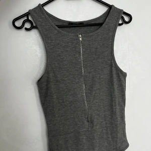 Grå ribbad linnetopp från Alcott - Säljer en snygg grå ribbad linnetopp från Alcott i storlek medium. Toppen har en dragkedja framtill som ger en cool detalj. Perfekt för en casual look eller att styla upp för fest!