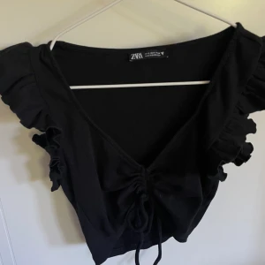 Topp - Säljer min fina svarta topp från Zara! Har volanger vid ärmarna och en snörning man kan knyta! Sparsamt använd och inga tecken på användning. Storlek S men passar även XS!💛