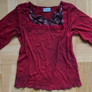 Röd tröja med spetsdetaljer från Motivi - Säljer en snygg röd tröja från Motivi med spetsdetaljer runt halsen och ärmsluten! Som man ser på bilderna så skiftar tröjan lite i mörkare och ljusare rött.