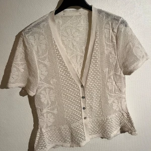 Broderad kofta  - Broderad, stickad kofta med korta ärmar. Färgen är offwhite. Pärlfärgade knappar. Superfin att ha som den är eller med ett linne under! Mycket gått skick och använd ett fåtal gånger. 