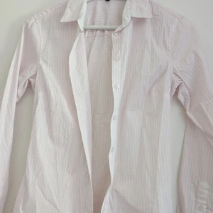 Långärmad skjorta 💘 - En jättefin vit,rosa randig skjorta i storlek XS (kvinna) kanske även skulle passa storlek S! Aldrig kommit till användning 💓 Såå fin till sommaren 🫶🏼