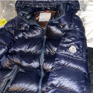 Blå dunjacka från Moncler - Snygg blå dunjacka från Moncler med dragkedja och fickor. Perfekt för kyliga dagar med sin pufferdesign som håller värmen. Om ni söker efter fler bilder är det bara att hojta till! Fick jackan i julklapp o morsan köpte från Plick så där av vet jag inte om den är äkta eller inte, ni kan höra av er o fråga så skickar jag bild men skulle faktiskt tro att den är äkta då den har tag  i loggan, serietidningen finns med vit hörna, storleken är i 1 och tagsen matchar. 