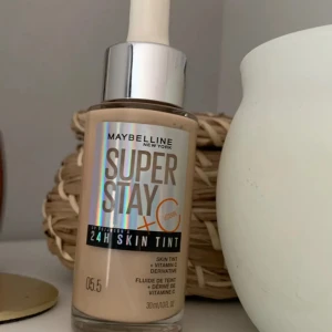 Maybelline Super Stay Skin Tint - Maybelline Super Stay 24H Skin Tint i nyansen 05.5. Denna foundation ger en lätt täckning och innehåller vitamin C för en fräsch och strålande hud. Perfekt för en naturlig look som håller hela dagen.