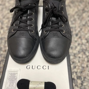 Gucci - Snygga svarta sneakers från Gucci med diskret mönster och snörning. Skorna har en stilren design med metallöljetter och är perfekta för en trendig look.