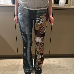 Jeans med mönster  - Säljer ett par coola jeans med unikt patchwork på ena benet och ett blekt mönster över hela byxan. De har en tight passform och är perfekta för dig som vill sticka ut. Jeansmaterialet är robust och de har en klassisk femficksdesign.