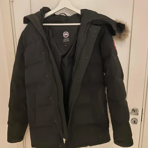 Svart dunjacka från Canada Goose (Riktig) - Säljer en svart dunjacka från Canada Goose med pälsdetaljer på huvan. Jackan är Perfekt för kalla vinterdagar. Den köptes för 13500 och den har aldrig använts eftersom den är för liten, kvitto kommer med. Pris kan diskuteras 😁