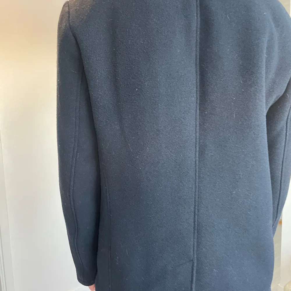 Snygg svart skepparkavaj från Armani Exchange i storlek M. Jackan har en klassisk dubbelknäppning med knappar och är tillverkad i en blandning av polyester och ull för en stilren look. Perfekt för kyligare dagar. Längd: 82 cm Bredd: 52 cm . Takit.