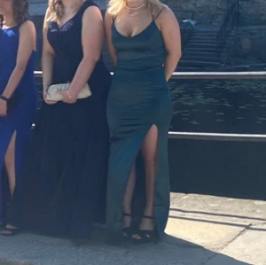 Mörkgrön långklänning med spetsdetaljer på ryggen  - Elegant mörkgrön långklänning med smala axelband och v-ringad spetsdetalj framtill. Klänningen har en slits och korsade band i ryggen, vilket ger en stilren look. Perfekt för festliga tillfällen. Säljer min mörk gröna satin klänning eftersom den inte kommer till användning. Endast använd på min bal, knappt använd. Pris går att diskutera. Den är från Bubbelroom 💕💕