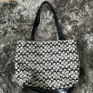 Mönstrad axelväska med svarta detaljer - Snygg axelväska med ett unikt mönster i svart och grå. Väskan har svarta handtag och en praktisk storlek för vardagsbruk. Perfekt för att bära med sig alla nödvändigheter.