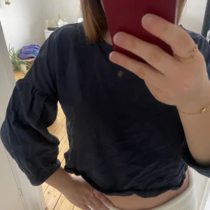 Marinblå blus med trekvartsärm - Snygg svart blus med trekvartsärm och puffiga ärmar. Perfekt för en stilren look. Blusen har en lös passform och är croppad, vilket ger en modern touch.