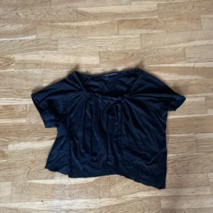 Svart blus med knytband - Säljer en svart blus med korta ärmar och knytband vid halsringningen. Blusen har en lös passform och är perfekt för en avslappnad stil.