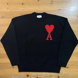 Svart tröja med rött hjärta från Ami - Snygg svart tröja från Ami paris med ett stort rött hjärta och bokstaven 'A' på bröstet. Tröjan har långa ärmar och ribbade muddar vid ärmslut och nederkant. Perfekt för en stilren look. Ny pris ligger på 6000