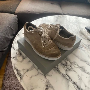 Beige sneakers från Polo Ralph lauren - Säljer ett par snygga beige sneakers från Polo Ralph lauren. Skorna har en klassisk design med snörning och en vit sula. Perfekta för en avslappnad stil. Den har en liten defekt på sulan men funkar att använda perfekt!