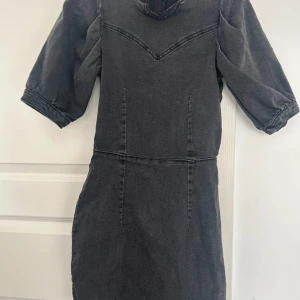 Svart klänning från H&M - Snygg svart klänning från H&M i jeansmaterial. Den har korta ärmar och en dragkedja baktill. Perfekt för en stilren look.
