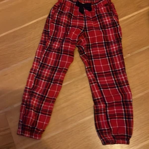 Röda rutiga byxor från KappAhl - Snygga röda byxor med rutig design från KappAhl. De har en bekväm elastisk midja och en dekorativ knytning framtill. Perfekta för en avslappnad stil.