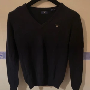 Svart tröja från Gant - Säljer en stilren svart tröja från Gant med v-ringning. Tröjan är tillverkad i ull och polyamid, vilket gör den både varm och hållbar. Perfekt för kyligare dagar.