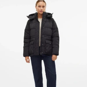 Svart pufferjacka med huva från vero Moda  - Snygg svart pufferjacka med huva och dragkedja. Jackan har långa ärmar och praktiska fickor framtill. Perfekt för kyliga dagar. Använt endast 2 gånger. 