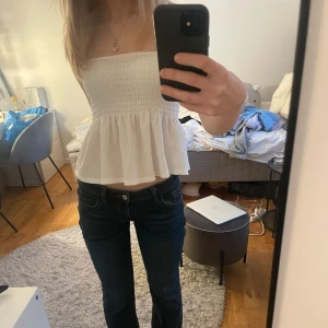 Vit axelbandslös topp från Gina Tricot - Säljer en söt vit axelbandslös topp från Gina Tricot. Toppen har en smockad överdel och en luftig, volangig nederdel. Perfekt för varma sommardagar eller en avslappnad dag på stan. 🌼