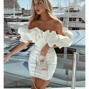 Vit axelbandslös klänning Dennis maglic  - Elegant vit axelbandslös klänning med volangdetaljer upptill. Den korta designen ger en stilren och modern look, perfekt för speciella tillfällen. Klänningen har en tight passform som framhäver figuren. Helt ny med lappen kvar fler finns pris går o diskuteras vid snabb affär perfekt till studenten ny pris 1499kr storlek M men sitter som S 