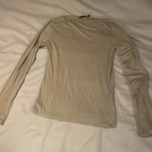 Beige långärmad tröja - Säljer en enkel och stilren beige långärmad tröja. Perfekt för lager-på-lager under kyligare dagar. Tröjan har en normal passform och är tillverkad i ett mjukt material.
