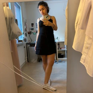 Svart spetsklänning - Snygg svart kortklänning med smala axelband och spetsdetaljer. Perfekt för en kväll ute eller en speciell tillställning. Klänningen har en figurnära passform som framhäver silhuetten.