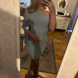 Ljusblå offshoulder klänning - Snygg ljusblå offshoulder klänning med en tight passform. Perfekt för en stilren look med en ärm och en axel bar. Klänningen är knälång och ger en elegant siluett.