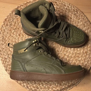 Gröna sneakers från Puma - Snygga gröna sneakers från Puma med hög modell och snörning. Skorna har en robust brun sula och är tillverkade i syntetmaterial. Perfekta för höst och vinter med sin varma insida.