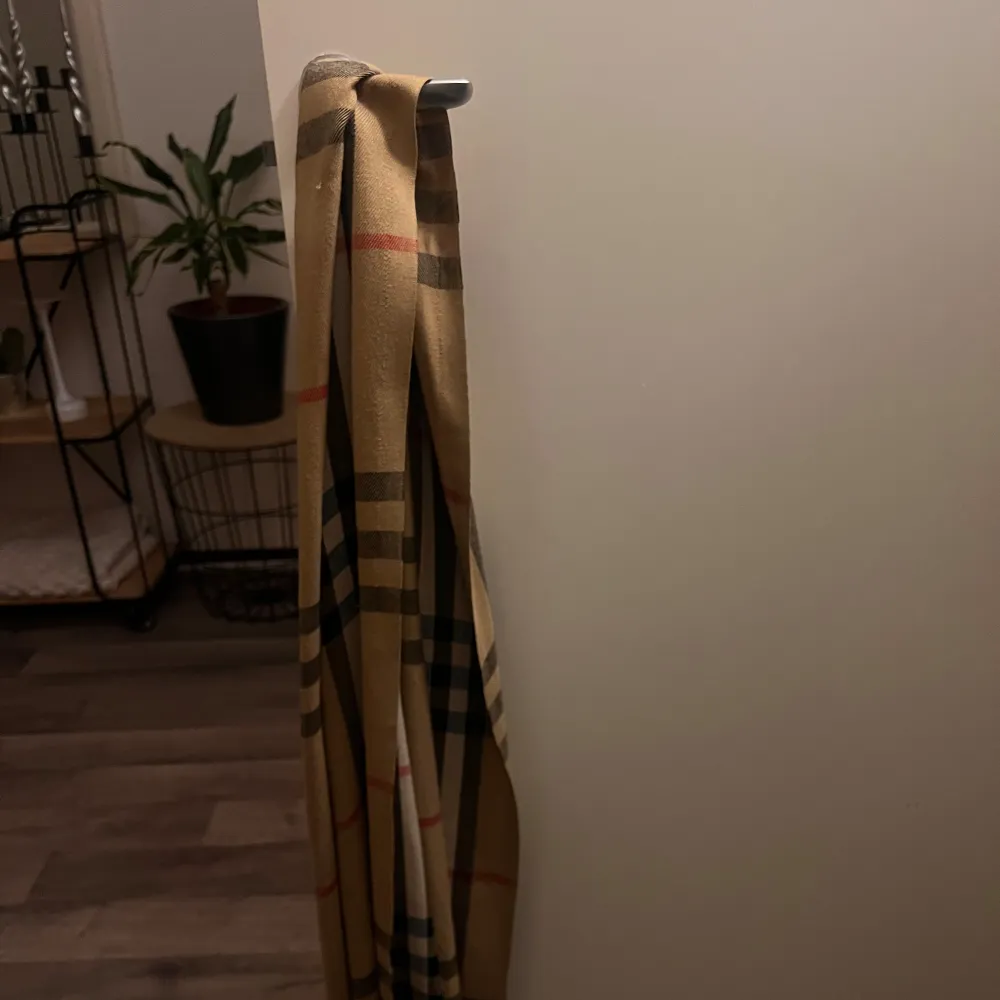 Snygg rutig halsduk i beige, svart och röd. Perfekt för att ge en klassisk touch till din outfit. Passar bra till kyligare dagar.. Muu.
