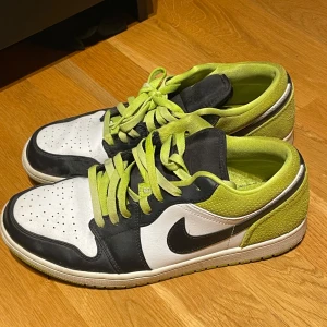 Nike Air Jordans med limegröna detaljer - Snygga Nike Air Jordans med en fräsch kombination av svart, vitt och limegrönt. Skorna har klassisk snörning och den ikoniska Nike-loggan på sidan. Perfekta för att ge din stil en färgklick. Strl 45.