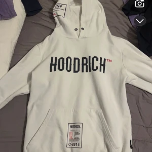 Vit hoodie från Hoodrich - Säljer en vit hoodie från Hoodrich med svart text på framsidan och en stor tryckt design på baksidan. 