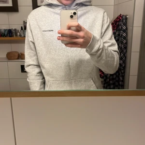 Grå hoodie från Axel Arigato - Säljer en stilren grå hoodie från Axel Arigato med tryck på bröstet. Den har en klassisk passform med långa ärmar och en praktisk magficka. Perfekt för en avslappnad look.
