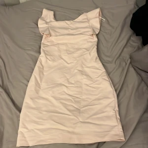 Ljusrosa klänning från ginatricot med volangdetaljer - Söt ljusrosa klänning med volangdetaljer vid ärmarna. Klänningen har en dragkedja i ryggen och en elegant, enkel design. Perfekt för en somrig look.